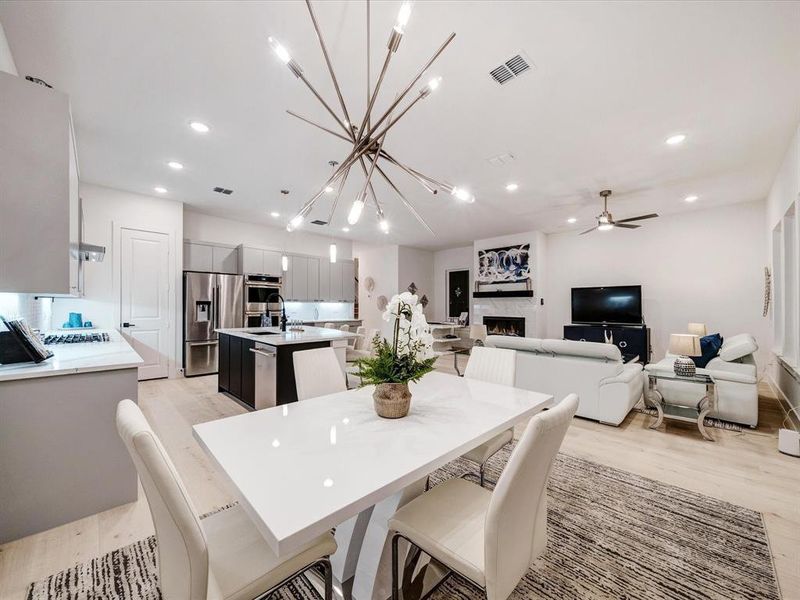 Dining space with a chandelier, light wood-style floors, a warm lit fireplace, recessed lighting, and a ceiling fan Dining space with a chandelier, light wood-style floors, a warm lit fireplace, recessed lighting, and a ceiling fan