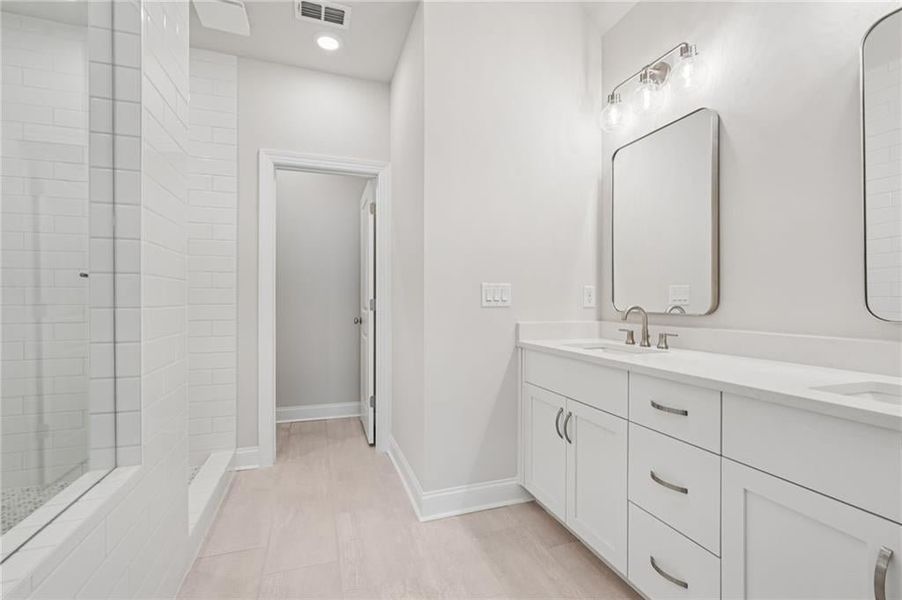 Bathroom featuring a tile shower, double vanity, and recessed lighting