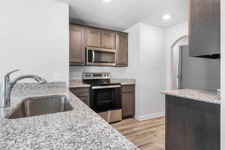 Kitchen with light stone countertops, appliances with stainless steel finishes, sink, and light hardwood / wood-style flooring