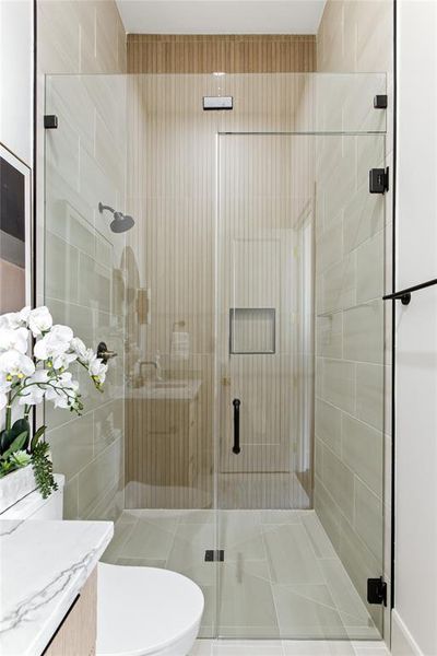 Glass-enclosed shower with a matte black shower head and integrated wall niche