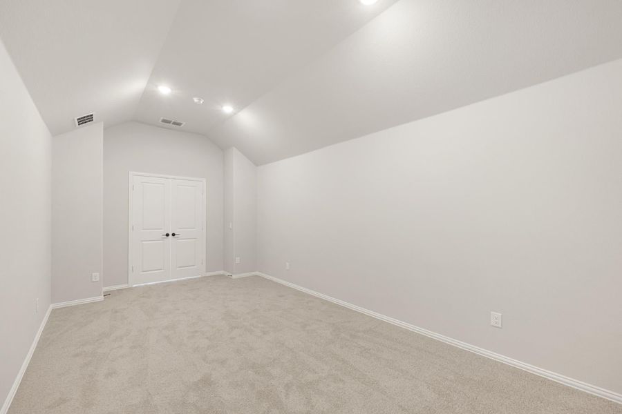 Empty bedroom with vaulted ceiling, recessed lighting, carpet flooring, and white double doors