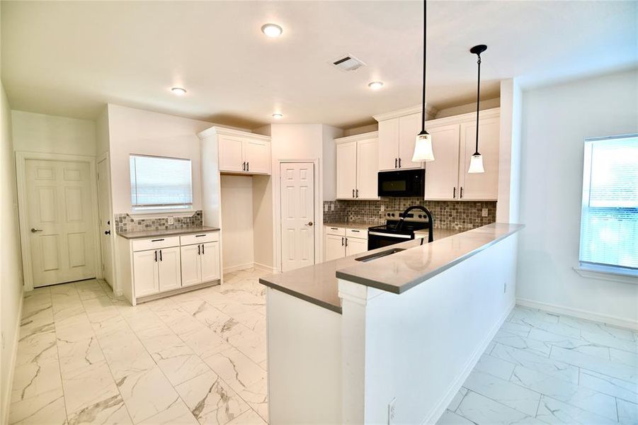 Kitchen with decorative backsplash, white cabinetry, stainless steel electric range, light tile patterned floors, and hanging light fixtures