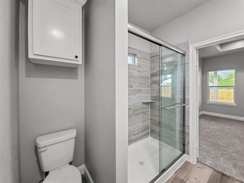 Bathroom with a stall shower, wood finished floors, toilet, and baseboards Bathroom with a stall shower, wood finished floors, toilet, and baseboards