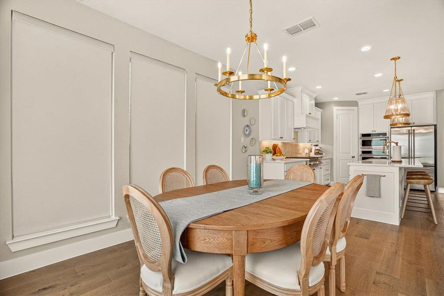 Dining area featuring a gold-finish chandelier, wood-finish flooring, and panel molding Dining area featuring a gold-finish chandelier, wood-finish flooring, and panel molding