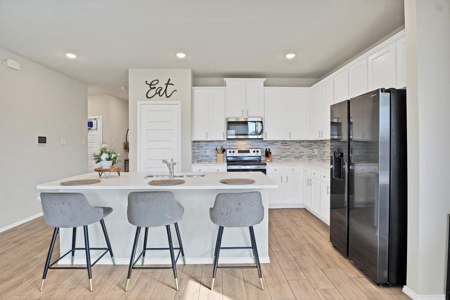 Kitchen with a center island with sink, sink, light wood-type flooring, appliances with stainless steel finishes, and white cabinetry