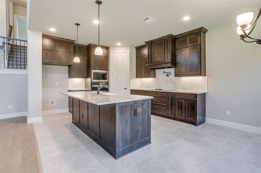 Kitchen with tasteful backsplash, light stone countertops, stainless steel microwave, hanging light fixtures, and stovetop