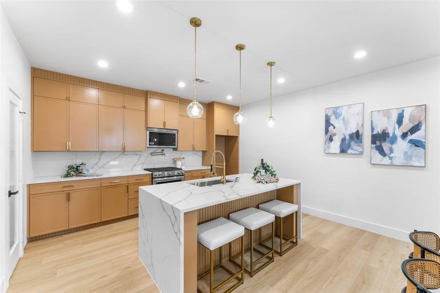 Kitchen featuring pendant lighting, a breakfast bar area, light wood-style floors, light stone countertops, and stainless steel appliances