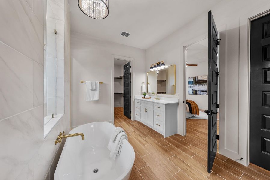 A spacious primary bathroom boasts a freestanding tub, sleek vanity, and warm wood-look flooring.