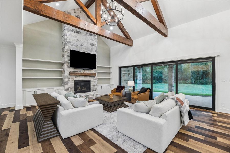 The great room is the heart of the home, where soaring vaulted ceilings and exposed wood trusses create a stunning architectural statement. A sophisticated linen-texture accent wall beautifully complements the custom-built shelving, adding warmth and designer appeal. Walls of glass fill the space with natural light, while the open layout seamlessly blends luxury, comfort, and timeless elegance—perfect for both entertaining and everyday living.