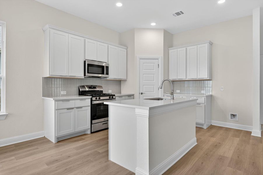 Kitchen featuring appliances with stainless steel finishes, white cabinets, decorative backsplash, a kitchen island with sink, and recessed lighting