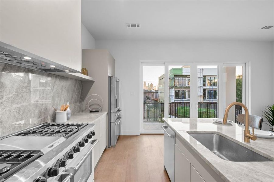 Kitchen featuring premium appliances, light stone counters, light wood-style flooring, white cabinetry, and decorative backsplash