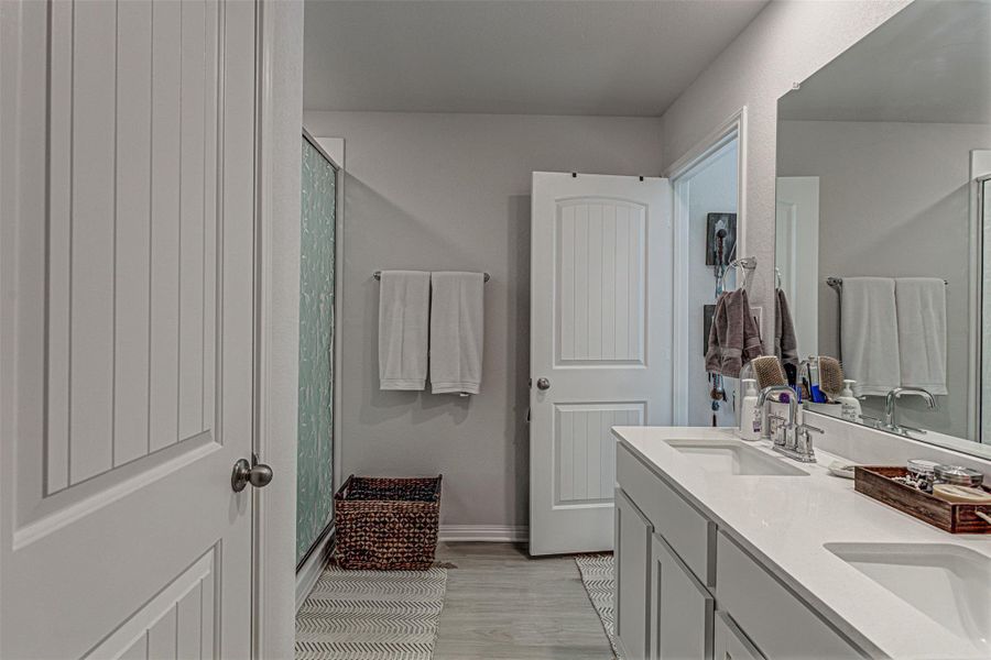 Full bathroom with a shower stall, double vanity, and light wood-type flooring