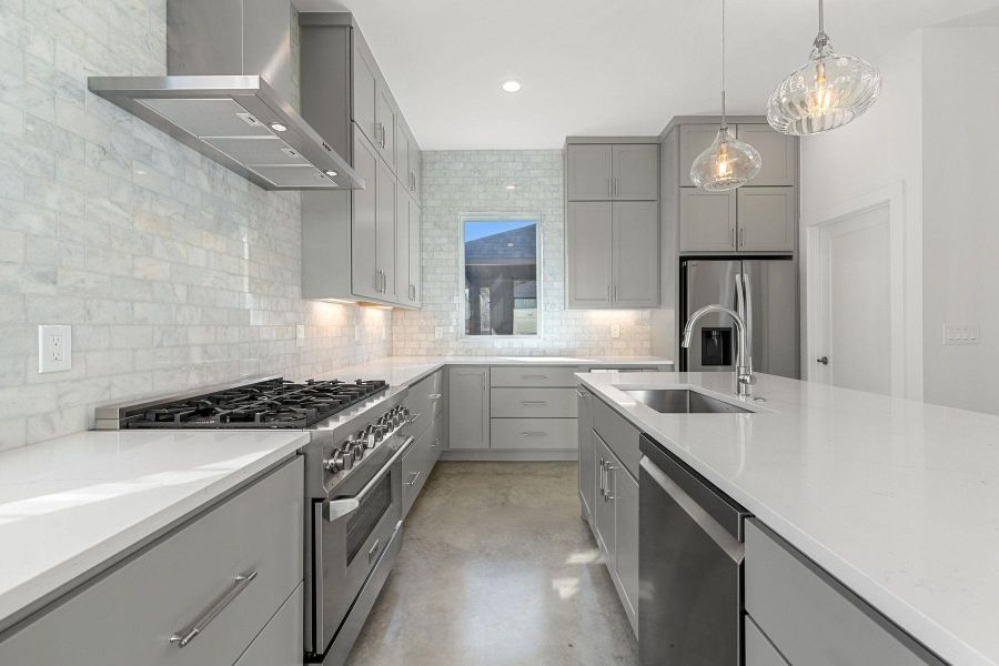 Kitchen with decorative backsplash, exhaust hood, stainless steel appliances, gray cabinetry, and a sink