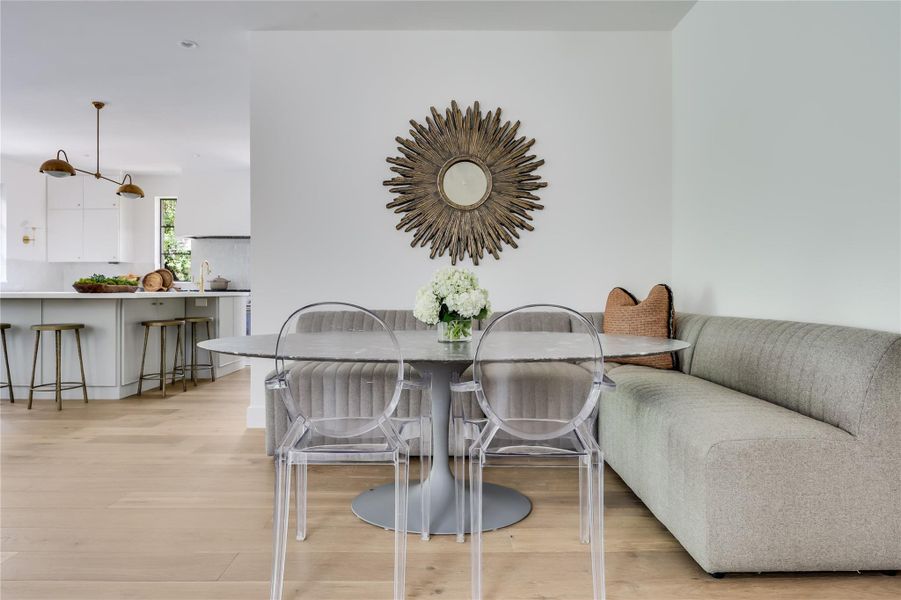 Open-concept dining area featuring light wood-finish flooring, a built-in upholstered banquette, and a decorative wall mirror