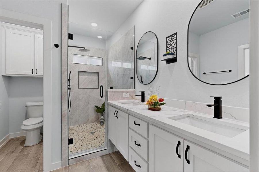 Bathroom featuring double vanity, a marble finish shower, and wood finish floors Bathroom featuring double vanity, a marble finish shower, and wood finish floors
