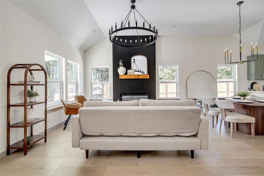 Living area with a chandelier, high vaulted ceiling, light wood-style flooring, and a large fireplace