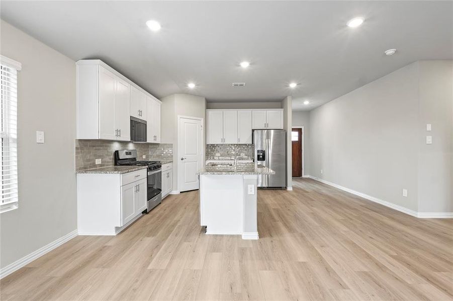 Kitchen with stainless steel appliances, tasteful backsplash, white cabinets, light wood-style flooring, and recessed lighting Kitchen with stainless steel appliances, tasteful backsplash, white cabinets, light wood-style flooring, and recessed lighting