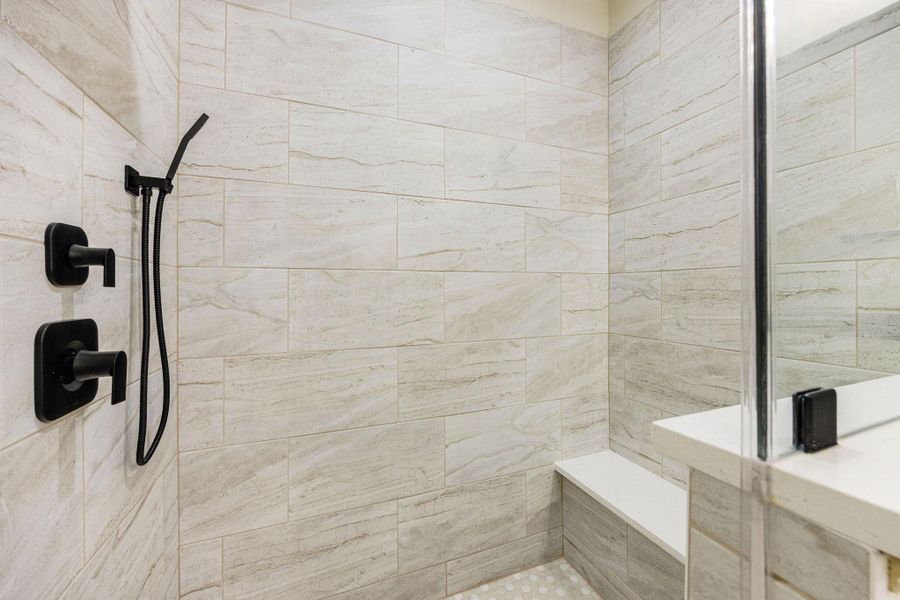 A modern shower with sleek, light stone tiles and matte black fixtures. It features a spacious design with a built-in bench, providing both style and functionality.