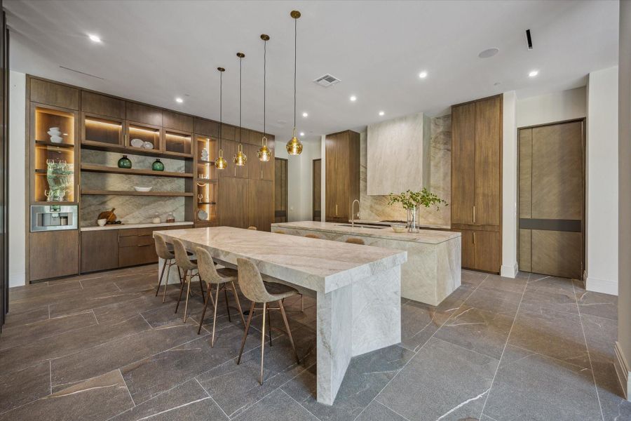 This showstopping designer kitchen blends sculptural beauty with top-tier performance. Dual islands wrapped in Taj Mahal Francini quartzite provide generous prep and dining space, complemented by custom cabinetry, illuminated display shelving, and elegant pendant lighting. A built-in Gaggenau coffee system and sleek hood surround add to the sophistication—while a fully equipped scullery kitchen is discreetly tucked behind, ensuring effortless entertaining and a clutter-free main space.
