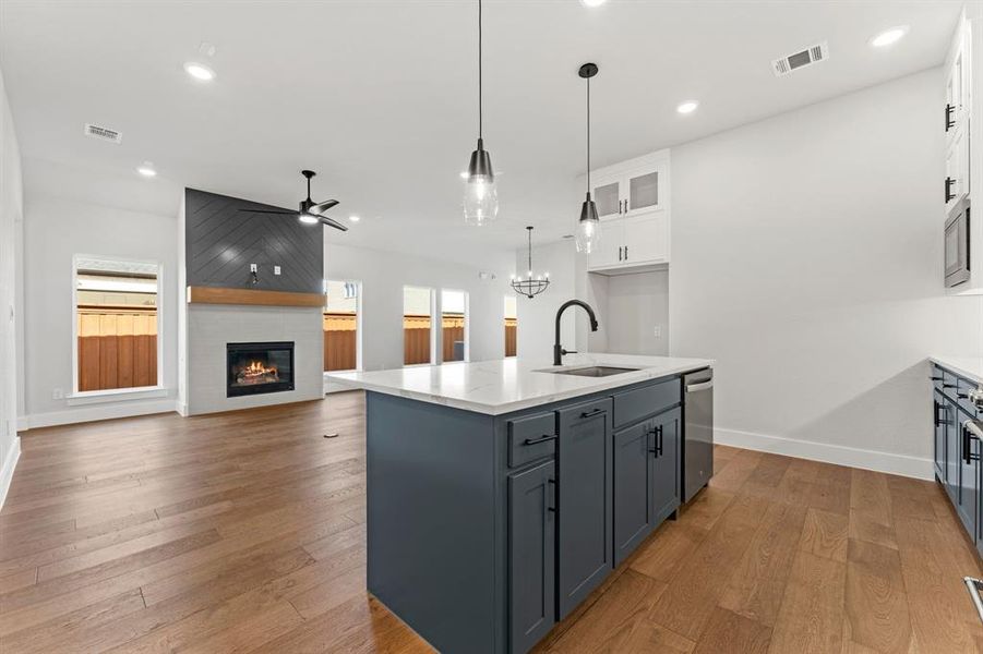 Kitchen featuring a kitchen island with sink, white cabinets, ceiling fan with notable chandelier, sink, and a large fireplace