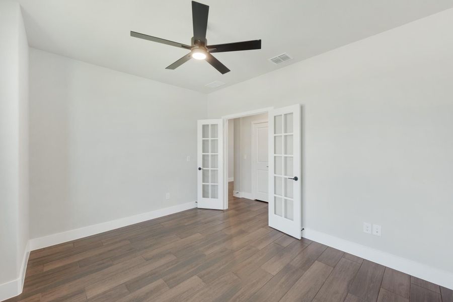 Empty room with dark hardwood floors, ceiling fan, and white French doors leading to hallway Empty room with dark hardwood floors, ceiling fan, and white French doors leading to hallway