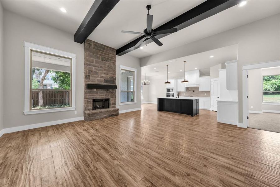 Unfurnished living room featuring a stone fireplace, light hardwood / wood-style floors, beamed ceiling, ceiling fan with notable chandelier, and sink