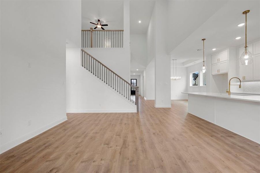 Open concept interior featuring light-toned flooring, a staircase with dark metal balusters, and a kitchen area with white cabinetry and a gold-toned faucet