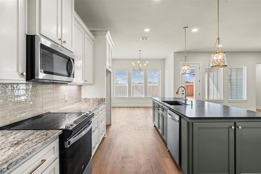 Kitchen featuring stainless steel appliances, white cabinetry, decorative light fixtures, recessed lighting, and a center island with sink