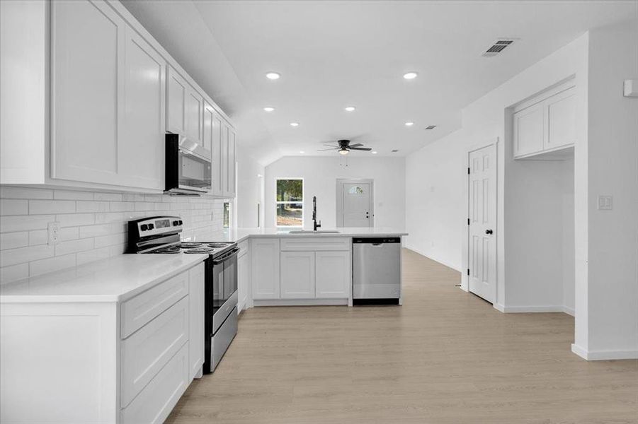 Kitchen featuring sink, stainless steel appliances, white cabinetry, and light hardwood / wood-style flooring