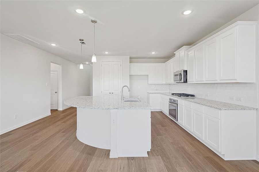 Kitchen featuring white cabinets, an island with sink, light stone countertops, pendant lighting, and light wood-style floors Kitchen featuring white cabinets, an island with sink, light stone countertops, pendant lighting, and light wood-style floors