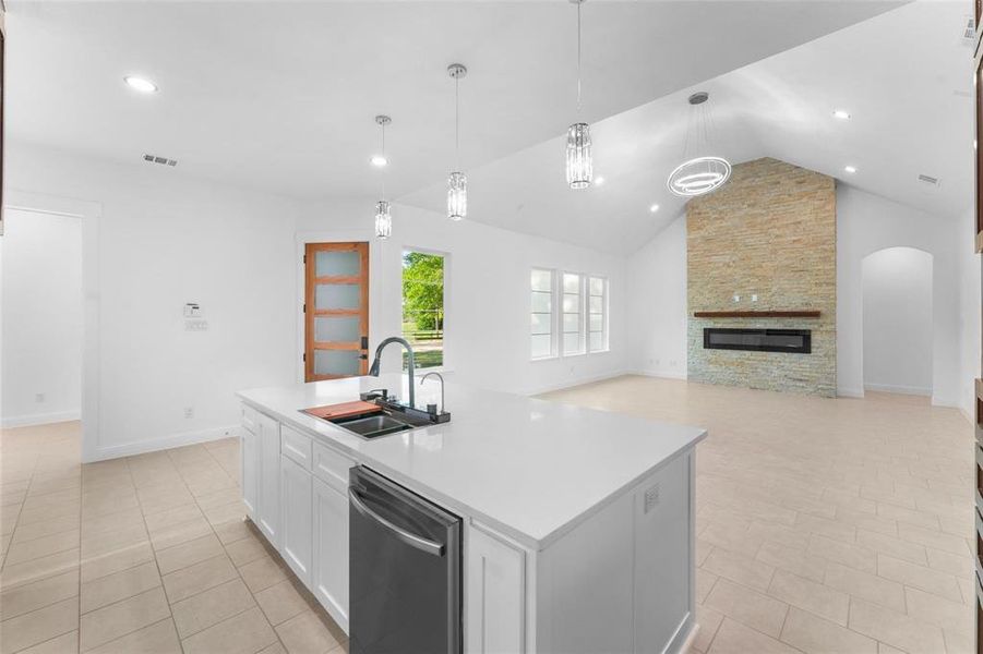 Kitchen with white cabinets, stainless steel dishwasher, high vaulted ceiling, open floor plan, and decorative light fixtures Kitchen with white cabinets, stainless steel dishwasher, high vaulted ceiling, open floor plan, and decorative light fixtures