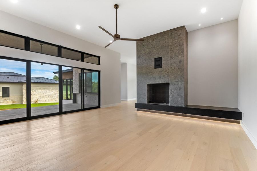 Unfurnished living room with a ceiling fan, a high ceiling, wood finished floors, baseboards, and a tiled fireplace Unfurnished living room with a ceiling fan, a high ceiling, wood finished floors, baseboards, and a tiled fireplace