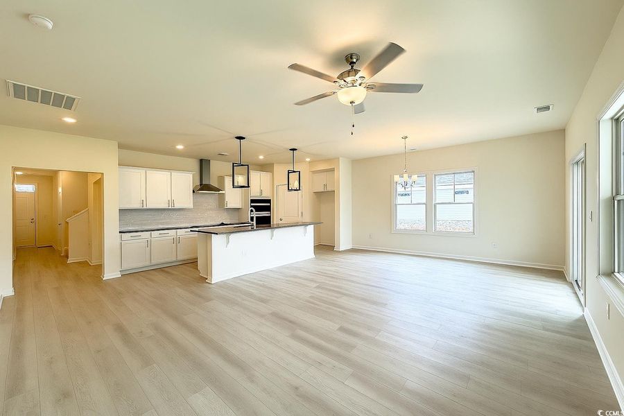 Kitchen with tasteful backsplash, white cabinetry, light wood-type flooring, dark countertops, and a chandelier Kitchen with tasteful backsplash, white cabinetry, light wood-type flooring, dark countertops, and a chandelier