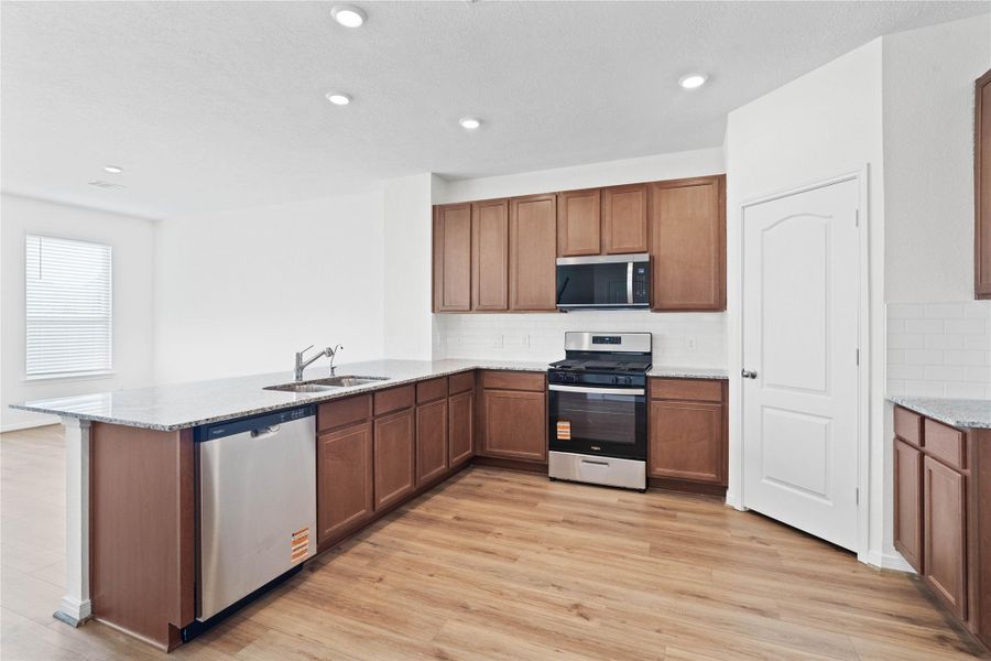 This spacious kitchen boasts soaring ceilings, Woodmont Cody cabinets in a Ginger stain, Granite Luna Pearl countertops, stainless steel Whirlpool appliances, a modern Daltile backsplash, recessed lighting, an extended breakfast bar countertop, and a pantry—all overlooking the expansive Great Room. This spacious kitchen boasts soaring ceilings, Woodmont Cody cabinets in a Ginger stain, Granite Luna Pearl countertops, stainless steel Whirlpool appliances, a modern Daltile backsplash, recessed lighting, an extended breakfast bar countertop, and a pantry—all overlooking the expansive Great Room.