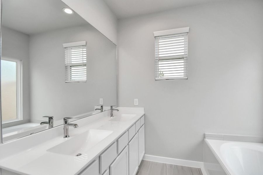 Elevate your daily routine at the refined vanity, now boasting double sinks, light-toned countertops, modern hardware, and bright recessed lights. Sample photo of completed home with similar floor plan. Actual colors and selections may vary.