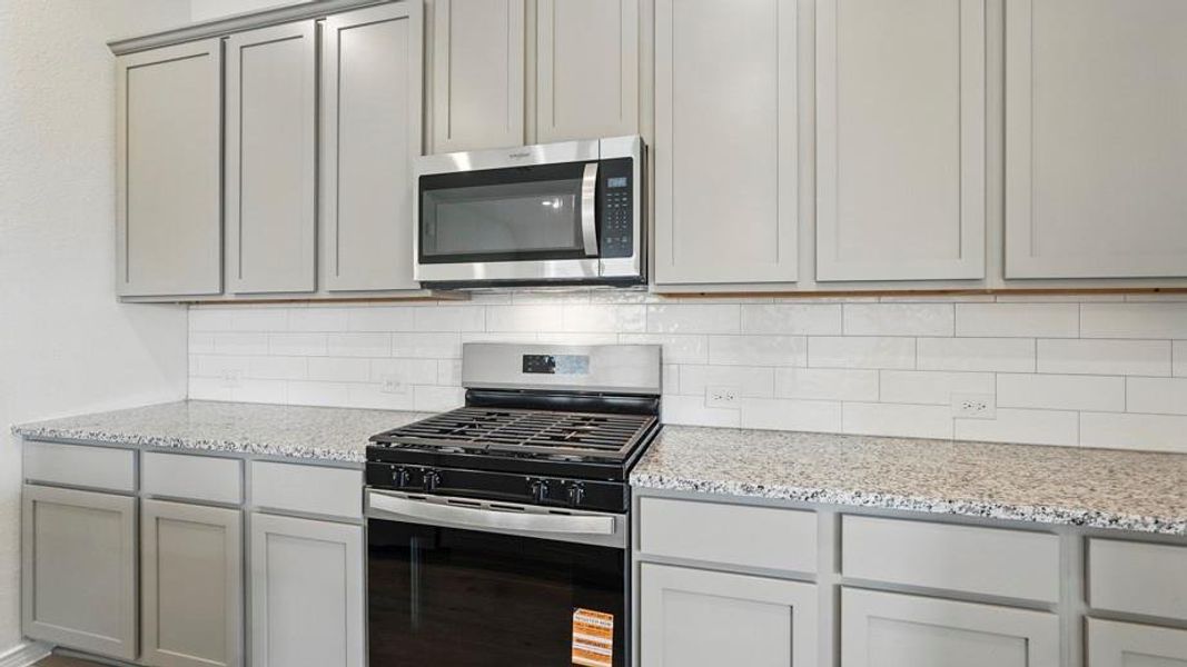 The kitchen features extensive light-toned cabinetry, granite countertops, and a subway tile backsplash