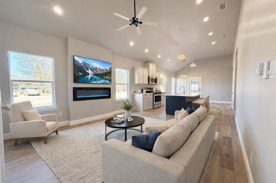 Living room with light wood finished floors, ceiling fan, vaulted ceiling, a glass covered fireplace, and recessed lighting Living room with light wood finished floors, ceiling fan, vaulted ceiling, a glass covered fireplace, and recessed lighting