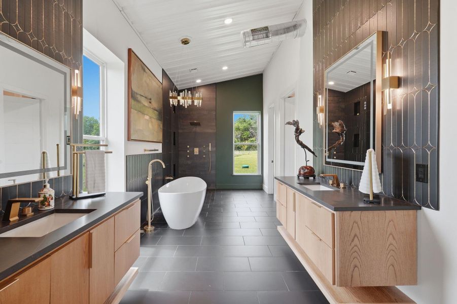 This bathroom features a modern design with sleek black tile flooring, dual wooden vanities with black countertops, and contemporary lighting. A freestanding bathtub sits centrally, with a large window offering natural light and views of greenery. The shower area is accented by dark tiles and a stylish chandelier.