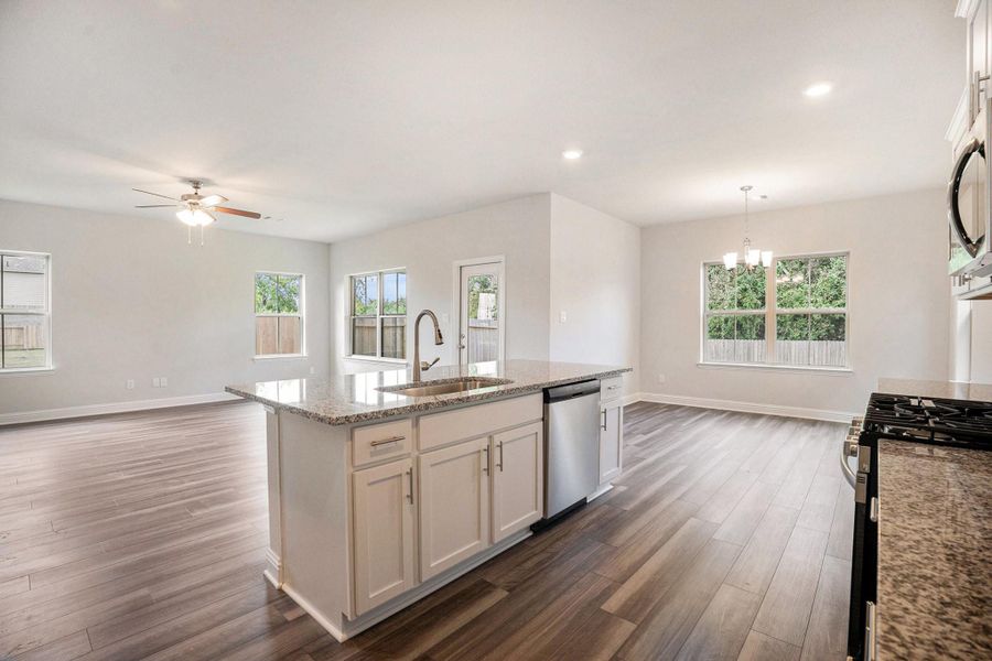 This photo showcases a spacious open-concept living area with a modern kitchen. It features granite countertops, stainless steel appliances, and a central island. The room has large windows allowing natural light and luxury vinyl plank flooring throughout.