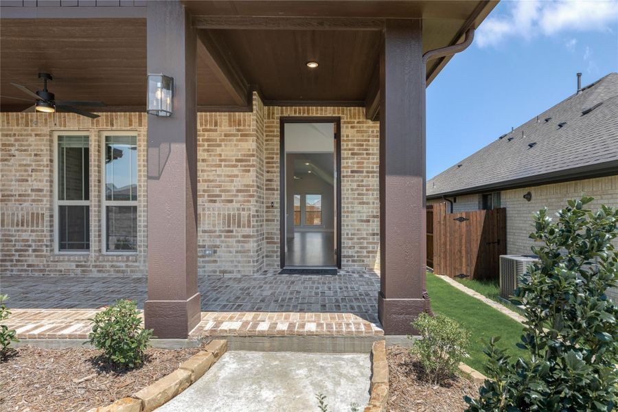 Covered front porch with brick exterior, glass front door, ceiling fan, and wall sconce light fixture Covered front porch with brick exterior, glass front door, ceiling fan, and wall sconce light fixture