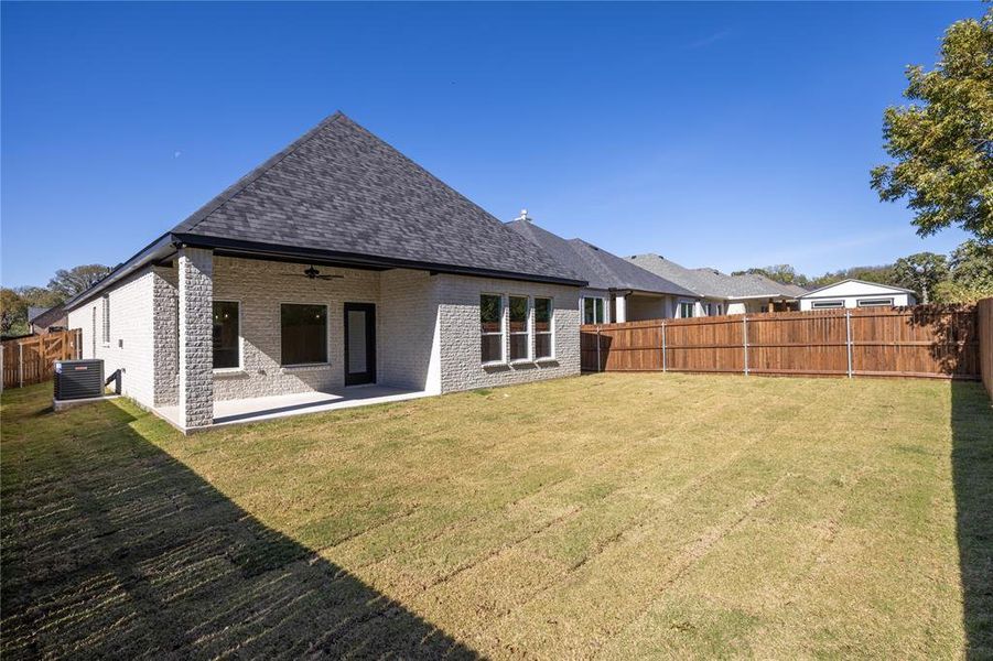 Rear view of house with a fenced backyard, brick siding, a patio area, roof with shingles, and a ceiling fan