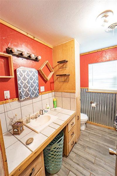 Bath featuring a textured wall, vanity, light wood-style floors