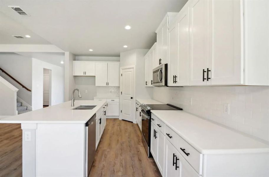 Kitchen featuring sink, appliances with stainless steel finishes, white cabinets, and a center island with sink