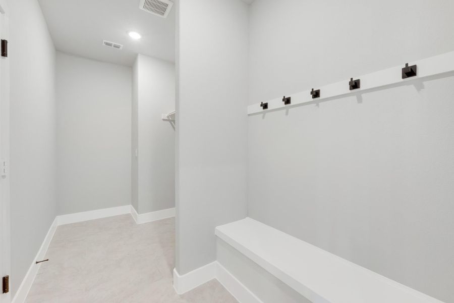 Mudroom with built-in bench, wall hooks, and hallway leading to closet with white walls