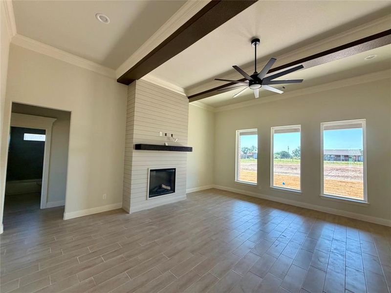 Unfurnished living room featuring ceiling fan, beam ceiling, wood tiled floors, a fireplace, and crown molding Unfurnished living room featuring ceiling fan, beam ceiling, wood tiled floors, a fireplace, and crown molding