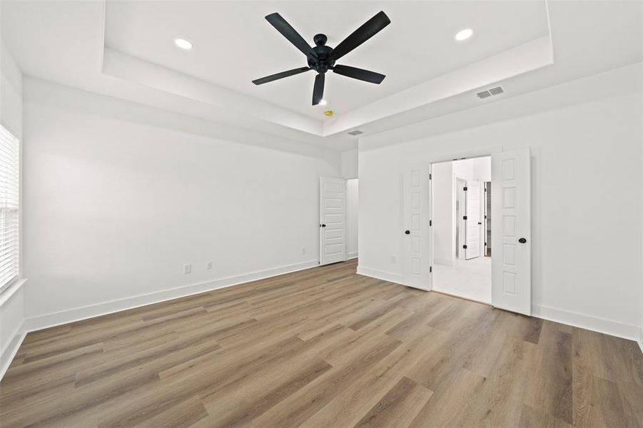 Unfurnished bedroom featuring ceiling fan, light wood-style floors, recessed lighting, and a raised ceiling