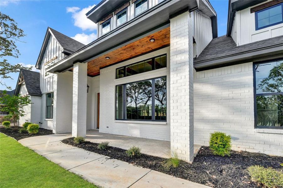 Entrance to property with brick siding, a porch, a shingled roof, and a yard Entrance to property with brick siding, a porch, a shingled roof, and a yard