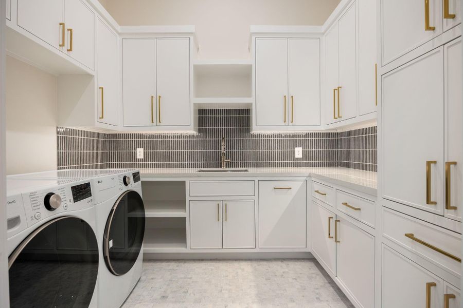 This beautifully appointed laundry room blends efficiency with elevated design, featuring extensive custom cabinetry, generous counter space, and a clean, cohesive layout. The neutral tones are complemented by warm hardware and subtle texture throughout. The highlight of this room is the abundant built-in storage and folding space, offering exceptional organization while maintaining a bright, polished environment that makes daily tasks feel seamless and refined.