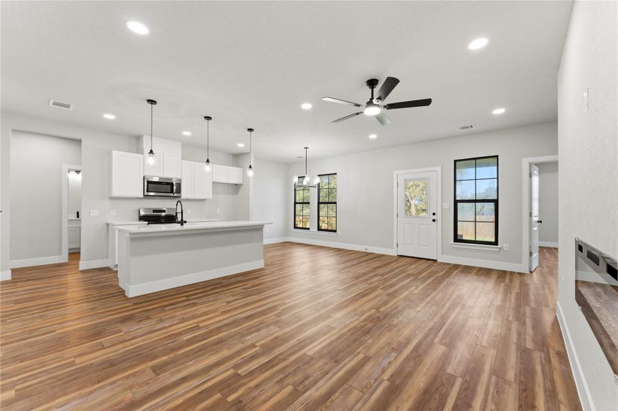 Unfurnished living room featuring ceiling fan, light wood finished floors, and a chandelier