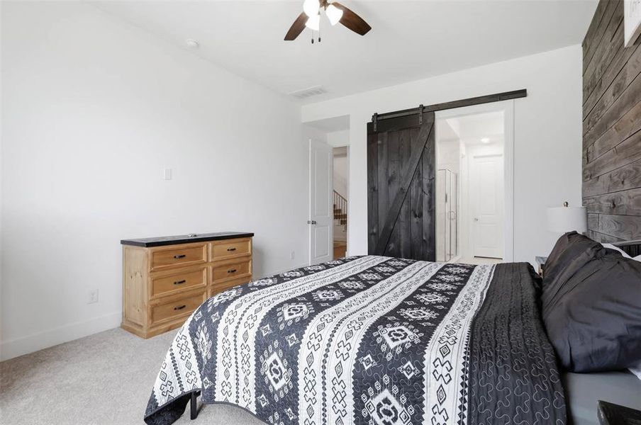 Spacious room featuring a dark wood barn door entry, a dark wood accent wall, and a ceiling fan